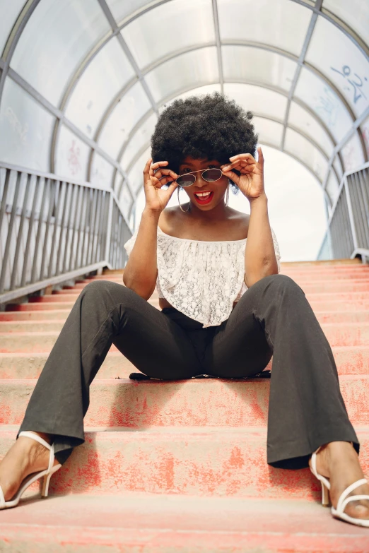 a woman in black and white blouse sitting on stairs with her hands behind her head