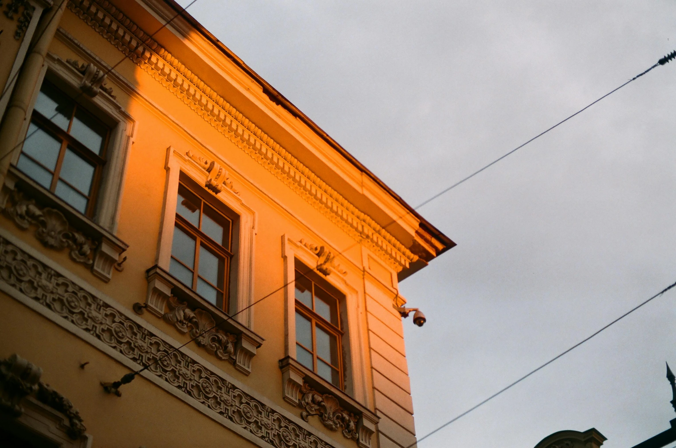 a yellow building on the street side with pigeons flying nearby