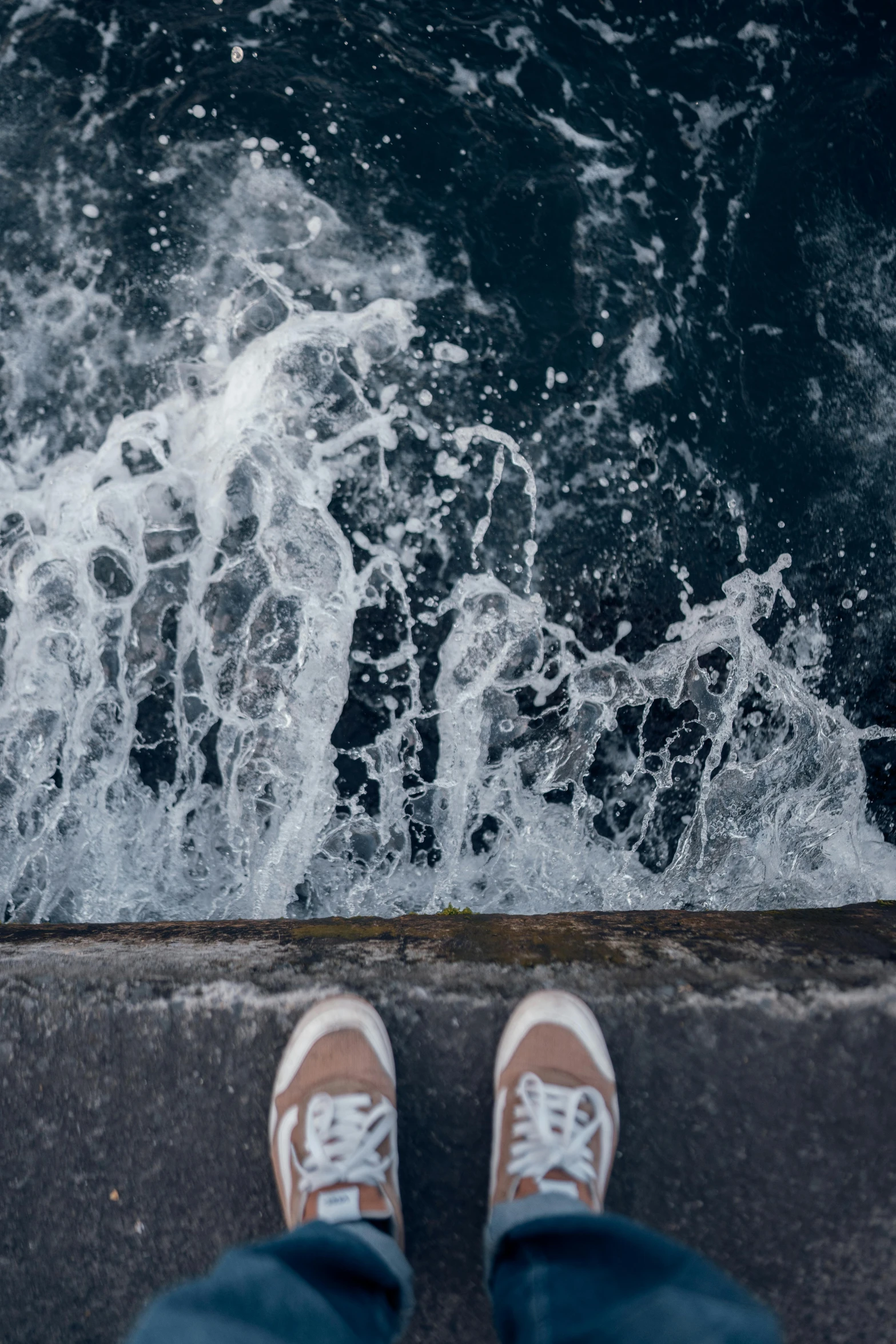 person in blue pants and white shoes standing in front of a body of water