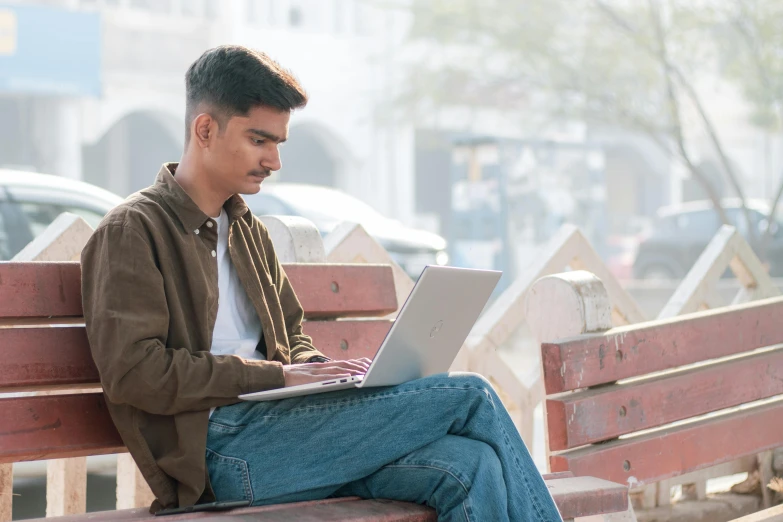 a young man sitting on a park bench using a laptop