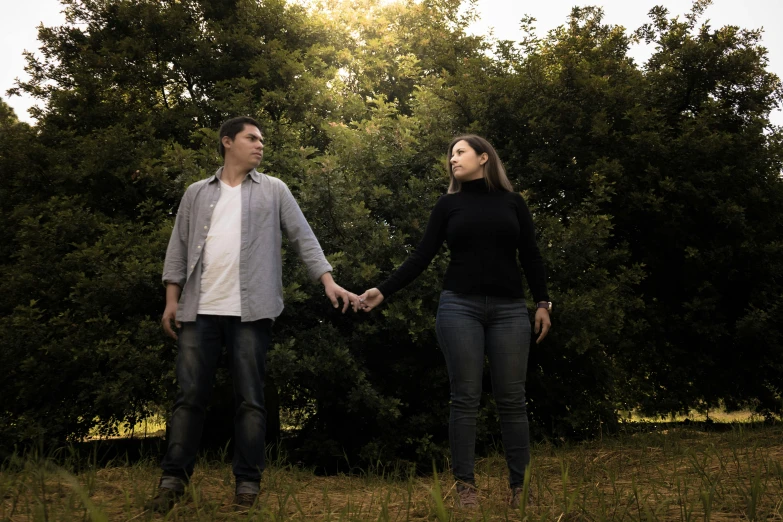 two people holding hands in a field surrounded by trees