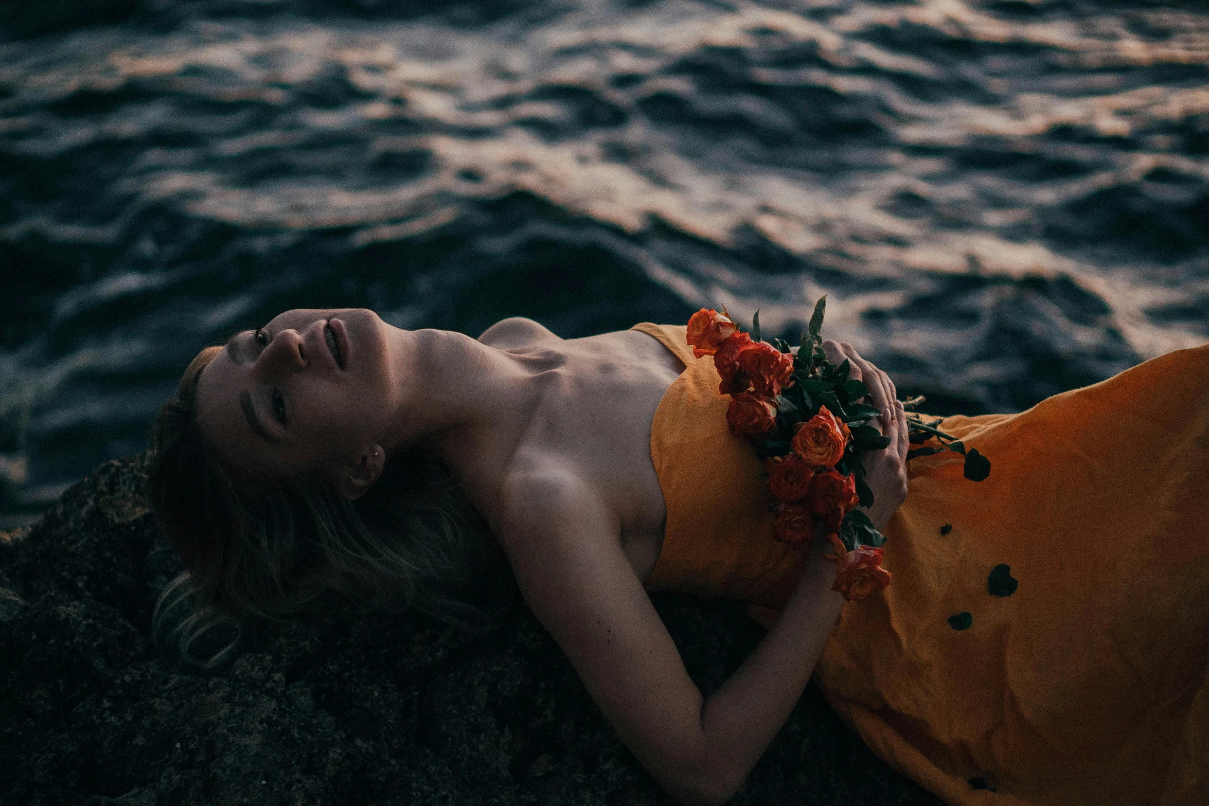 a woman with flowers on her head is lying by the water