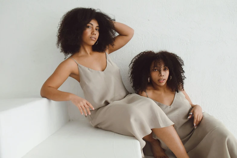 two women are posing on white furniture with their hands behind their backs
