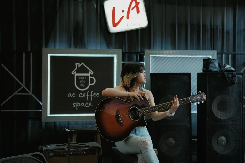 the girl with the guitar sits on stage playing