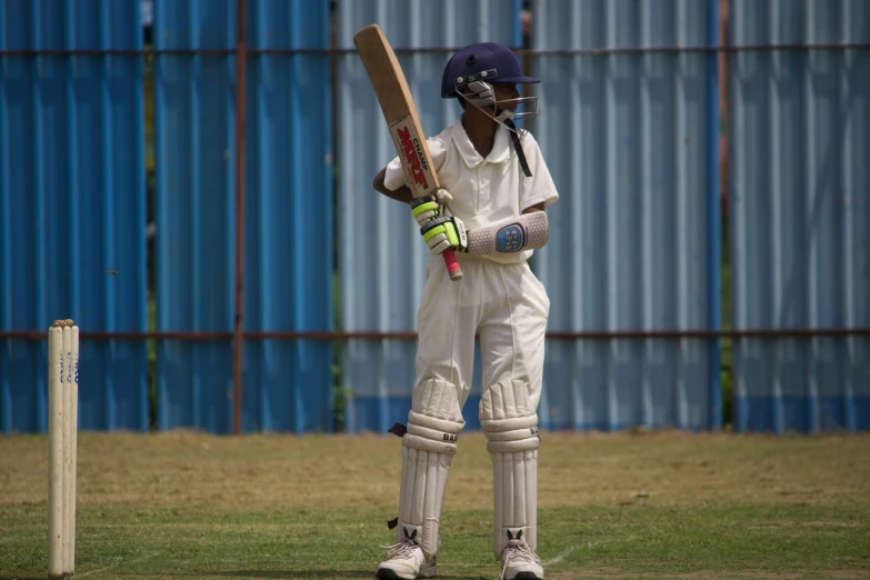 the man stands in a white uniform and holds a bat