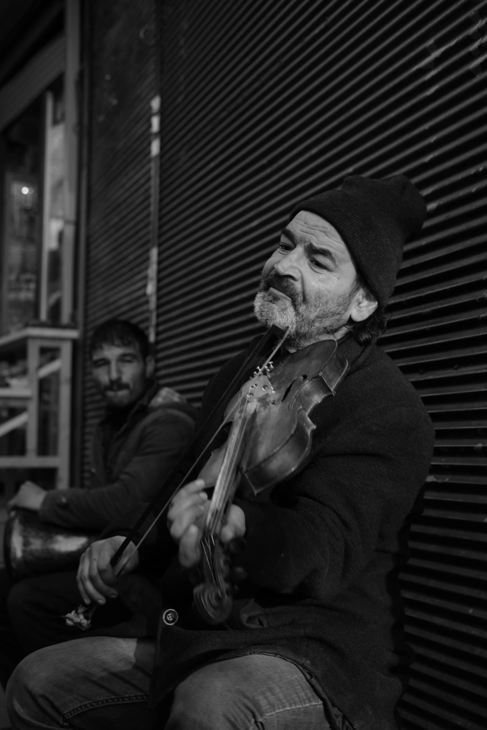 two men sitting on the sidewalk and playing instruments