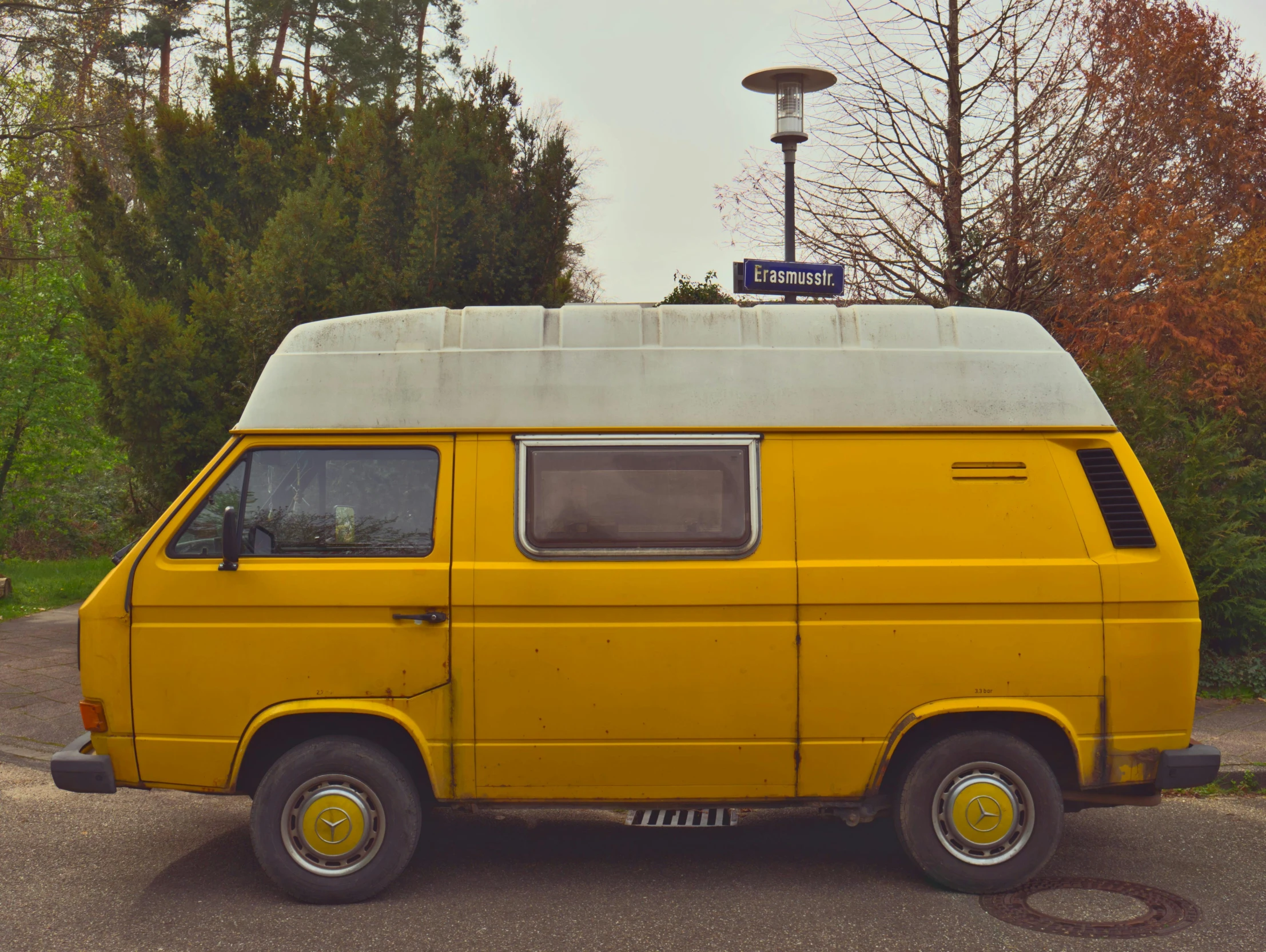 a yellow van with a surfboard on the roof sits in a parking lot