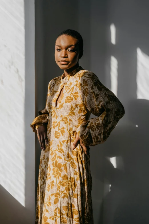 a woman stands in front of a white wall with a brown and yellow dress