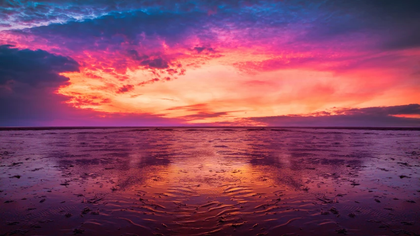 colorful sunset reflected in water on beach at ocean