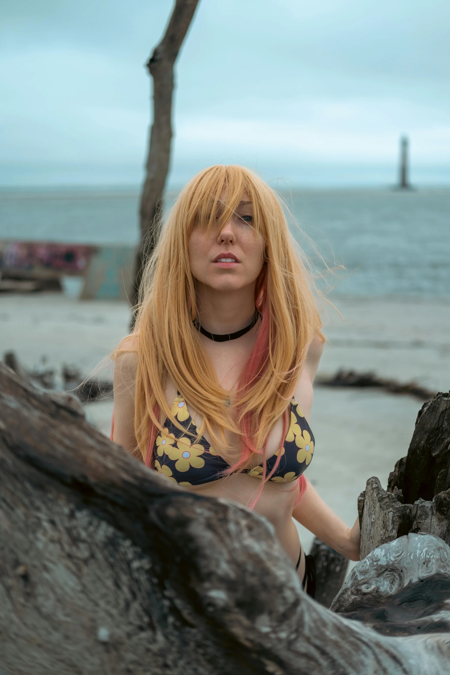 a woman with red hair and a black choker looking down while standing on the beach