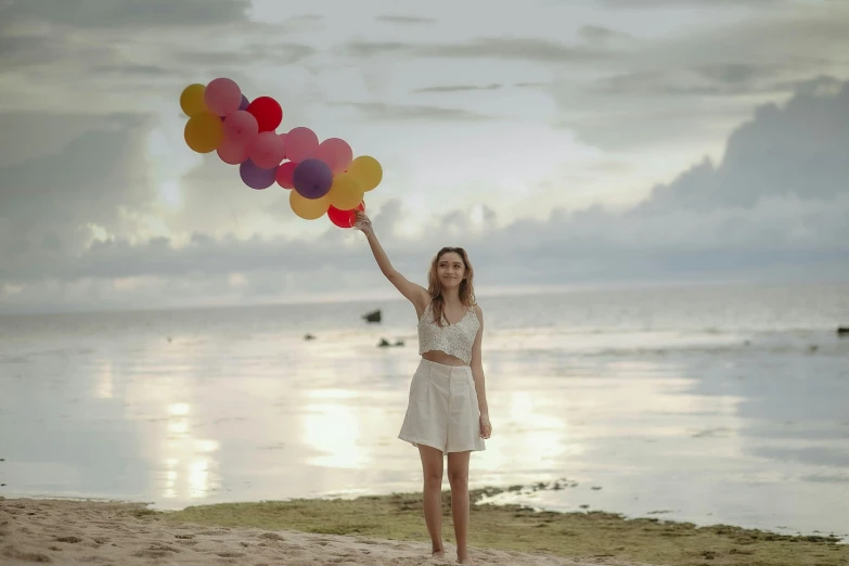 girl on the beach holding balloons up in the air