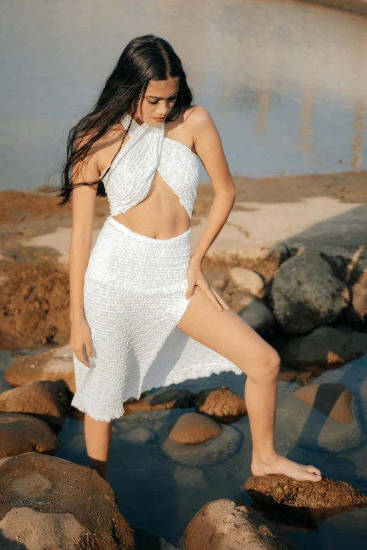 a woman in a white bodysuit is posed by rocks