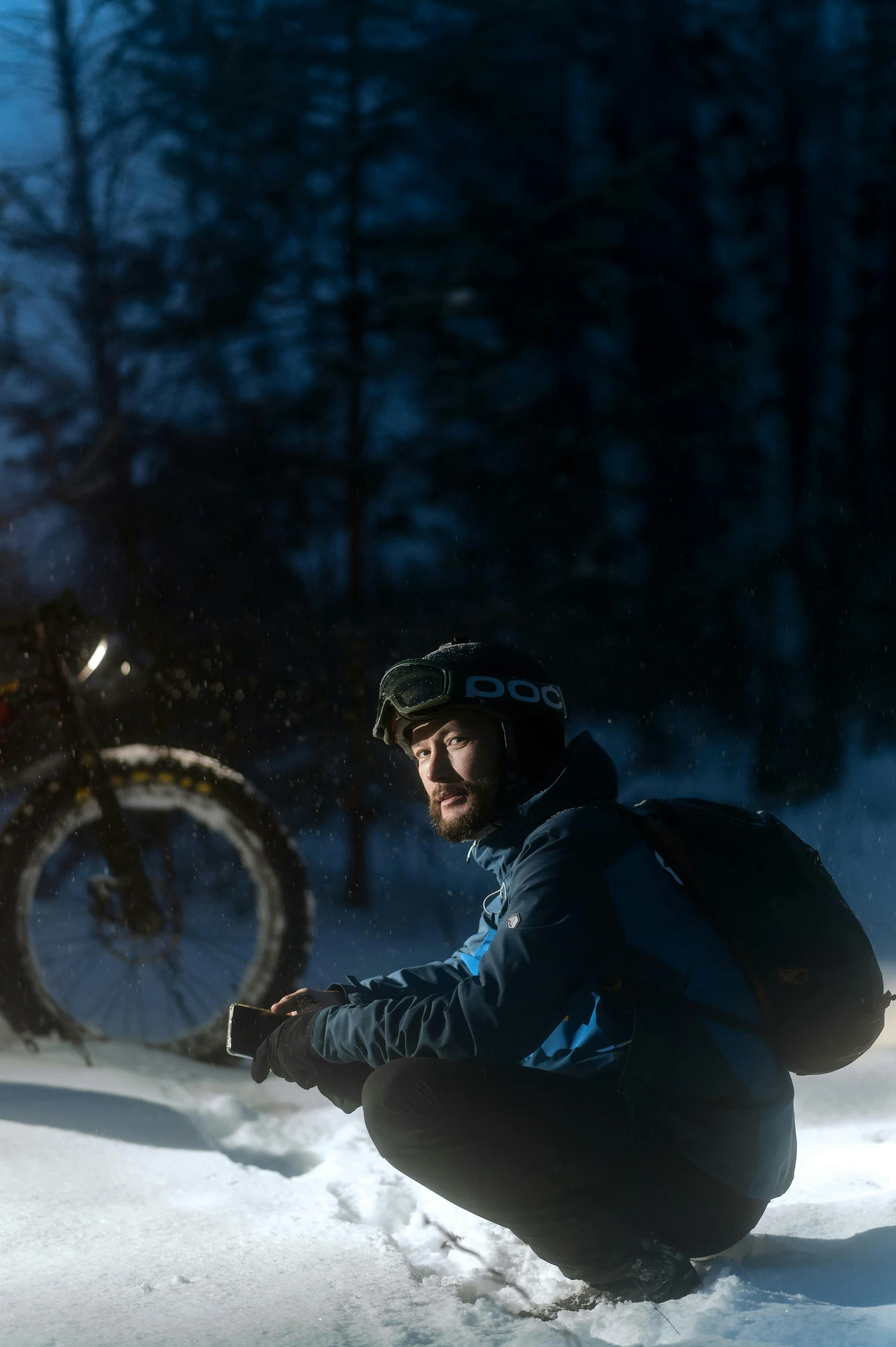 a man crouching down on the snow with a bike in the background