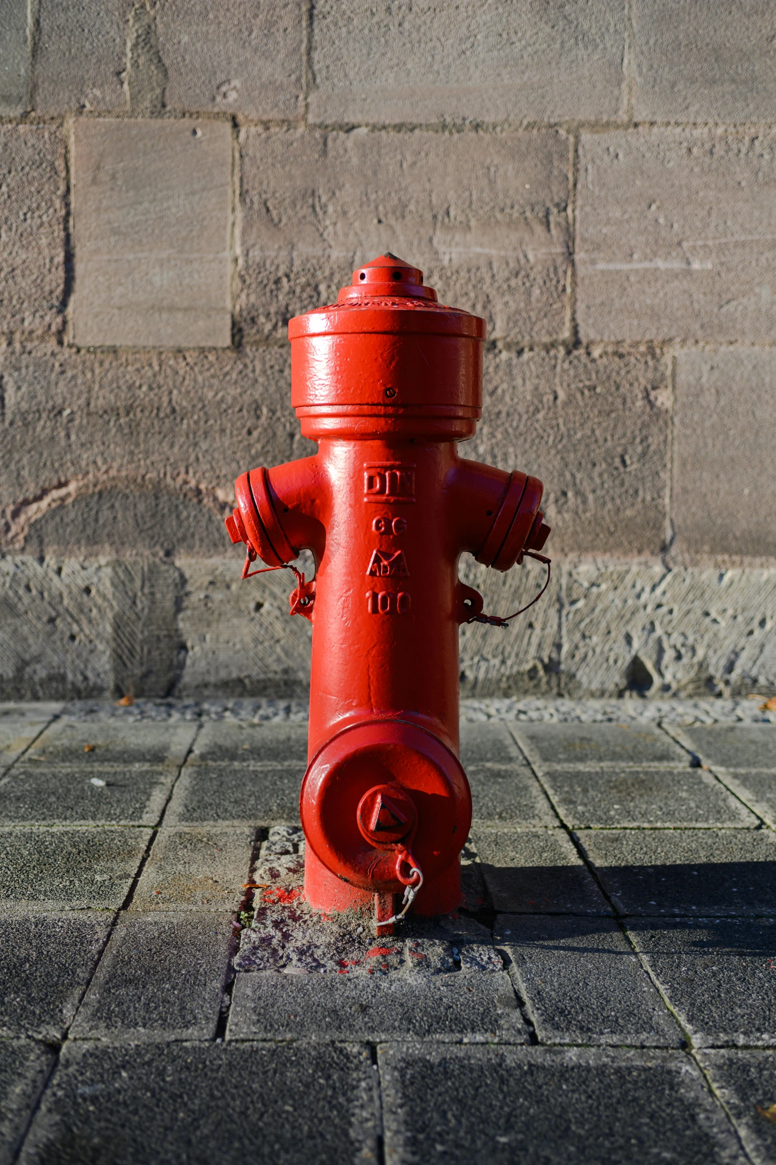 a red fire hydrant on pavement next to a brick wall