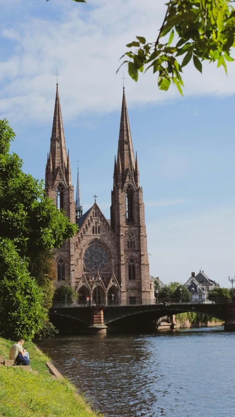 a couple sitting on the banks of a river under a cathedral