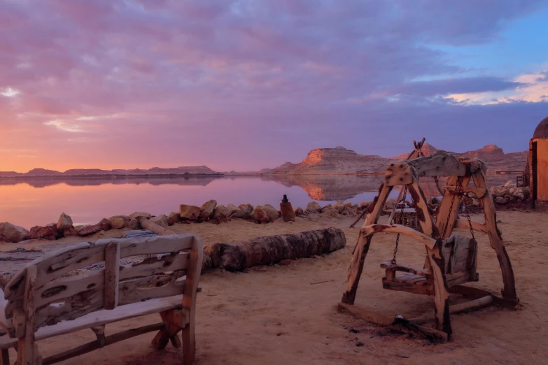 a wooden bench and swings in front of a lake at sunset