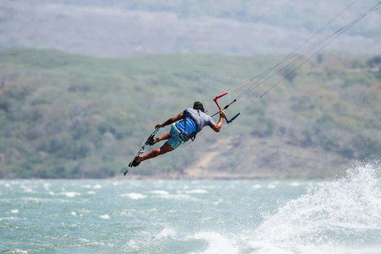 a man kiteboarding on some water in front of a green hillside