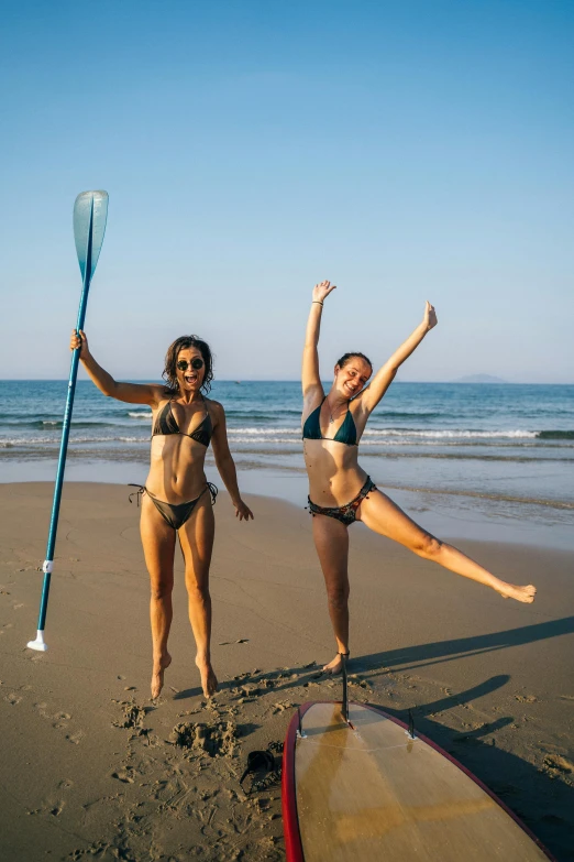 two women standing on beach next to a paddle