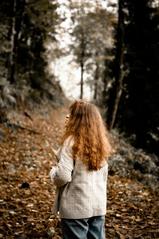 woman with red hair walking along a path in the woods