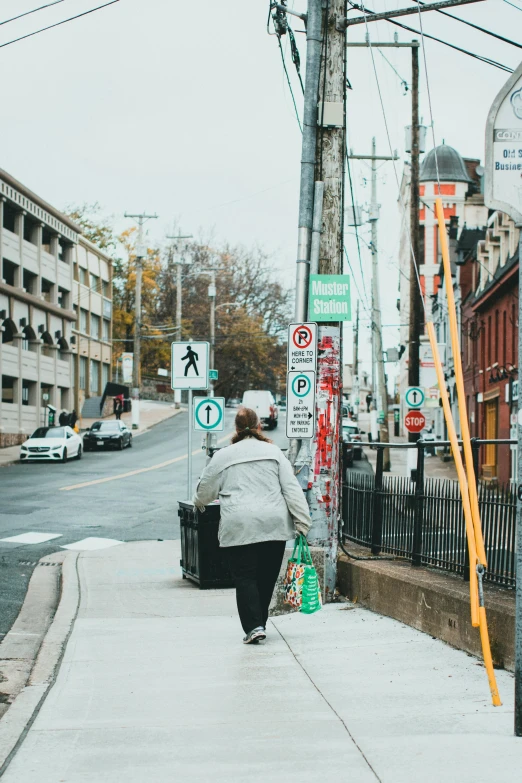 woman walking down street carrying items near cars