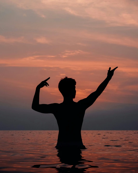 man on beach standing in calm water raising his arms to the sky