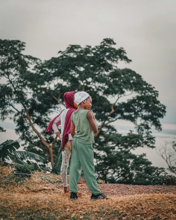 two children are standing near a tree and a cloudy sky