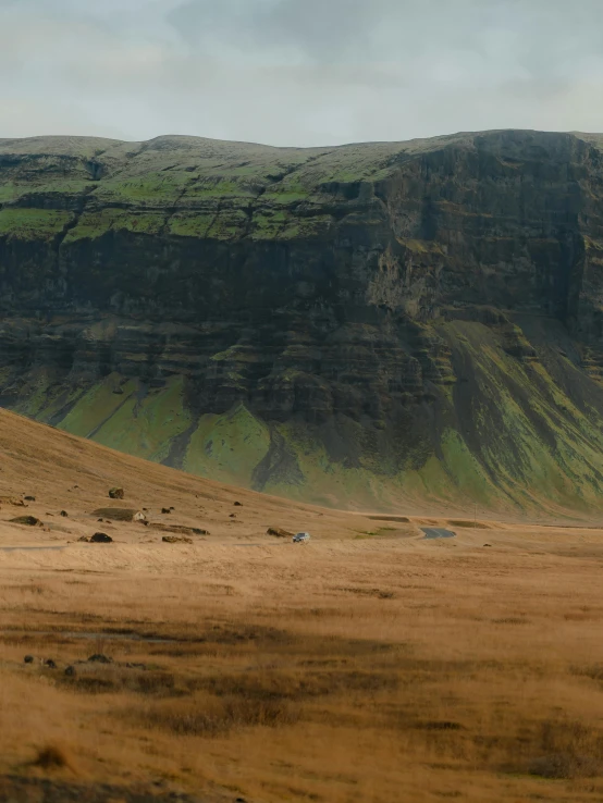 a large cliff sitting next to a hill covered in grass