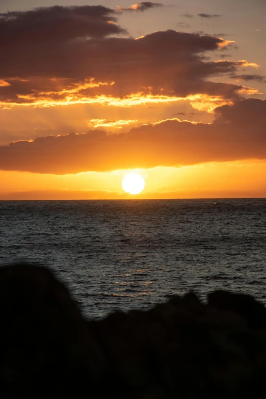 sunset with very clouds over calm water, silhouetted by dark silhouette