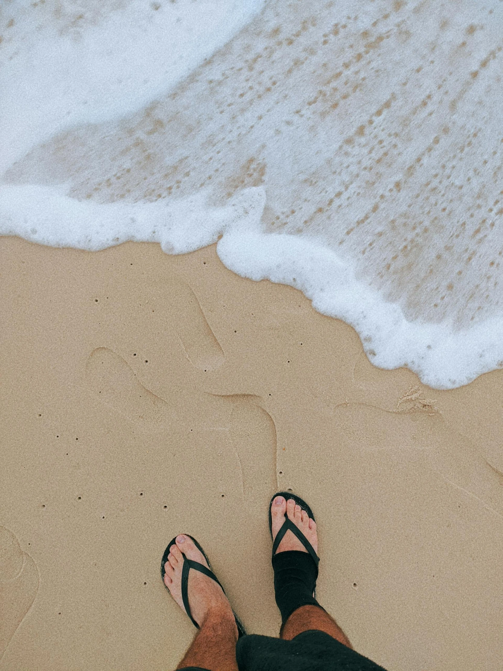 feet in sandals stand on the sand of the beach