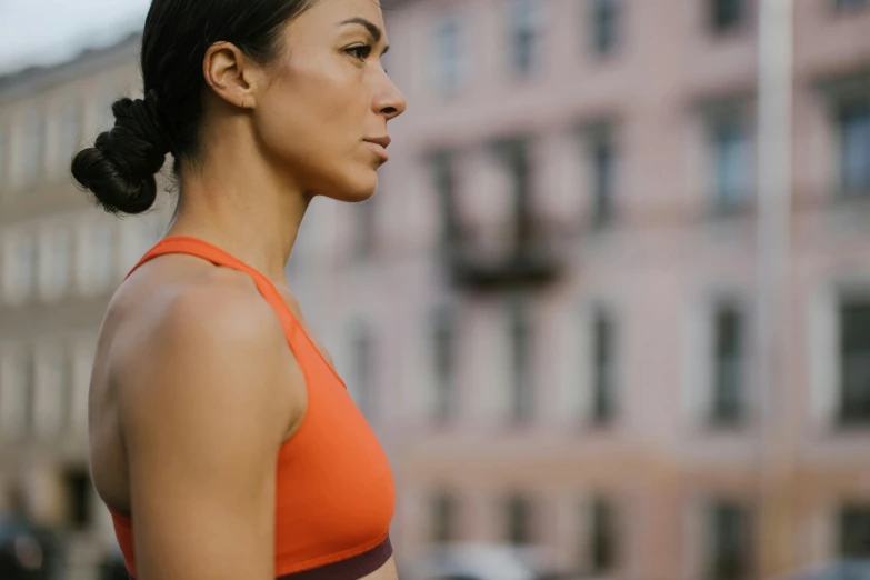 the woman wearing an orange top is standing in front of a large brick building