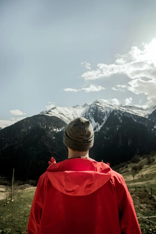 man wearing red rain coat in front of mountains