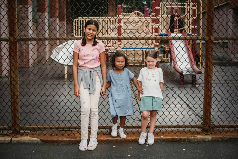 an older woman and two young children are standing next to a chain link fence