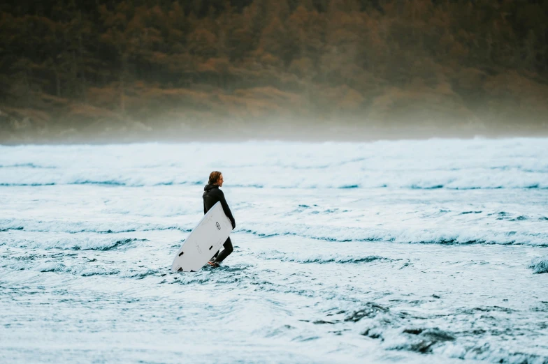 the man is walking into the ocean holding his surfboard