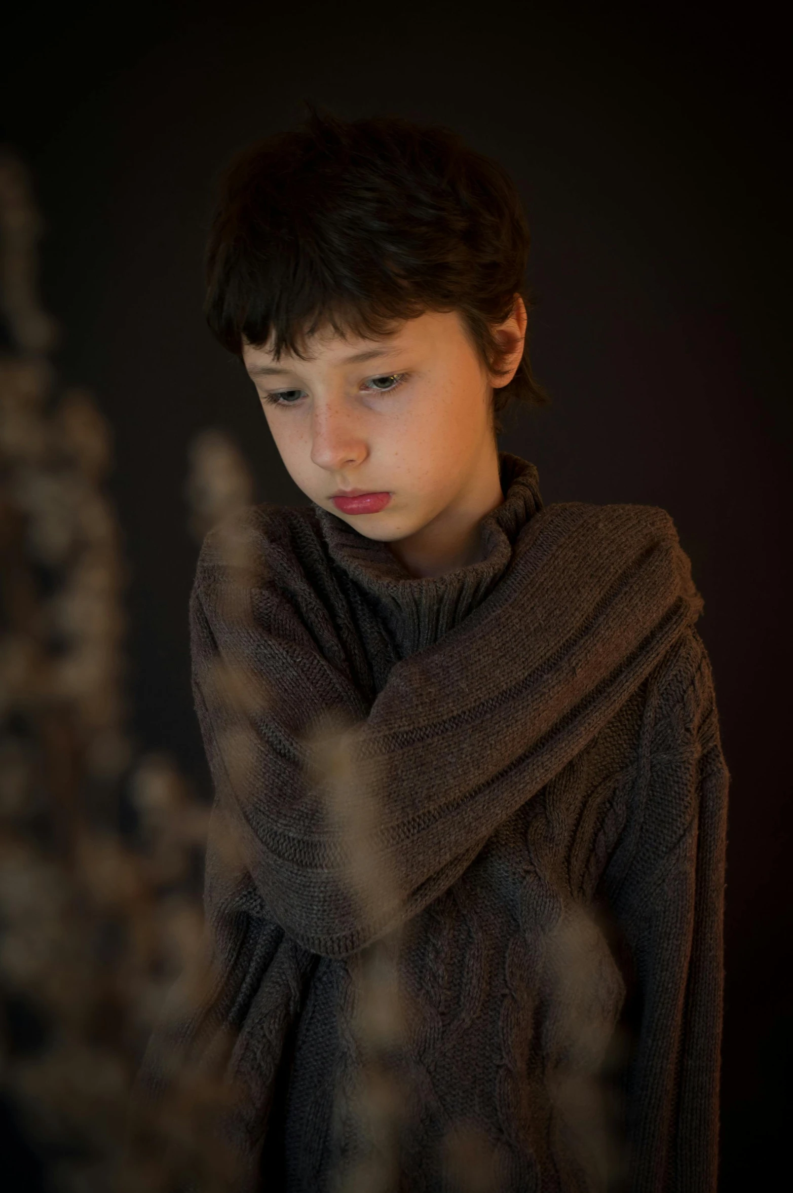 a boy in a brown sweater stares into the camera