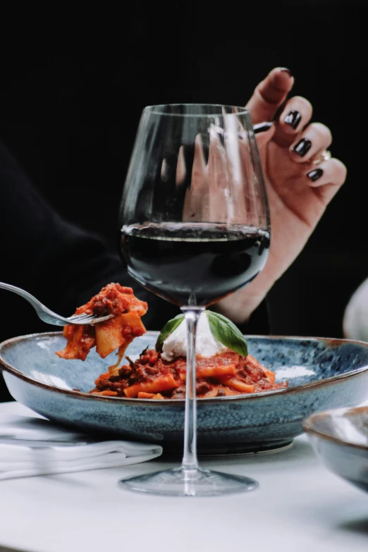 a hand holding a fork with pasta and wine