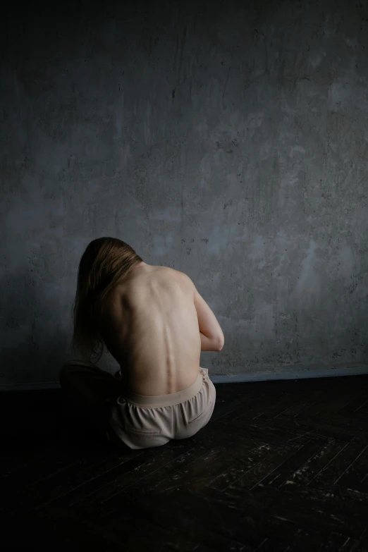 a shirtless man sitting down on a wooden floor