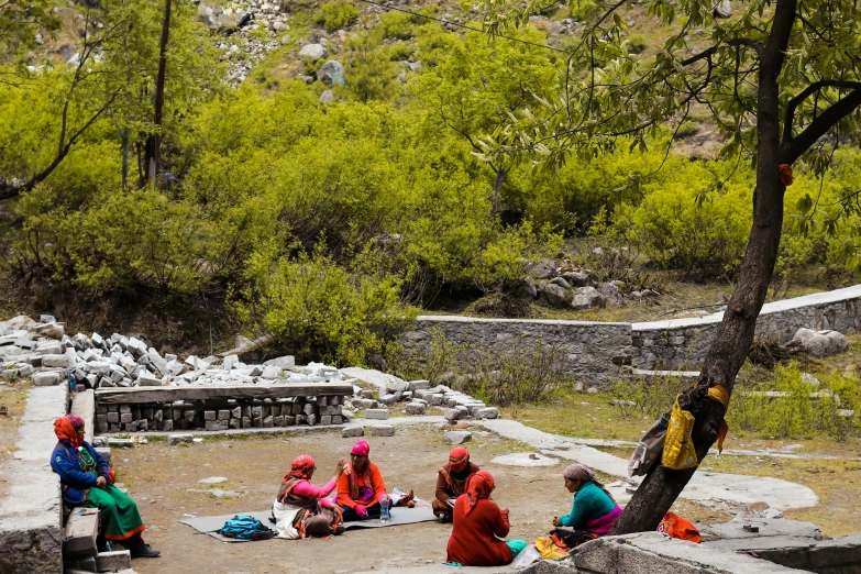 a group of people sitting and standing around a stone bench near a tree