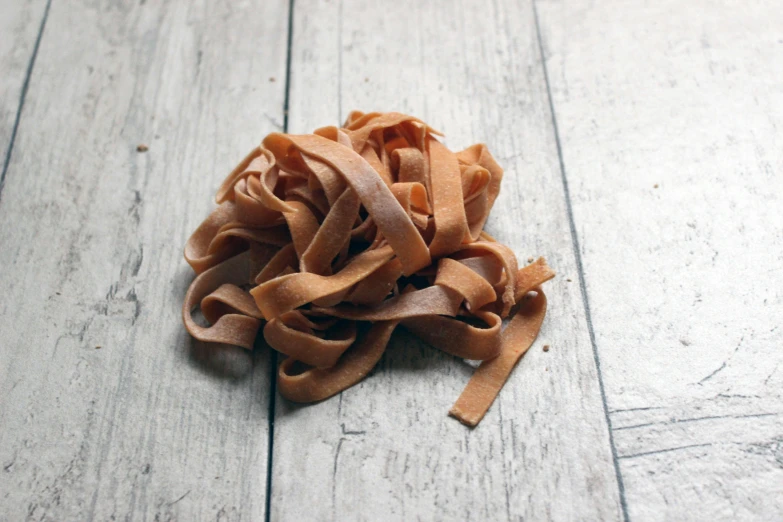 a pile of brown pasta noodles is laying on a wooden floor