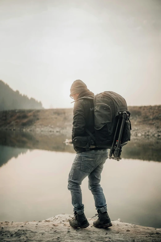 the guy is holding a backpack by the water