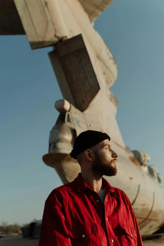 a man with beard and red shirt standing in front of a very large plane