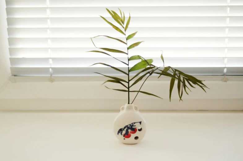 a white vase with a plant inside sits in front of a window