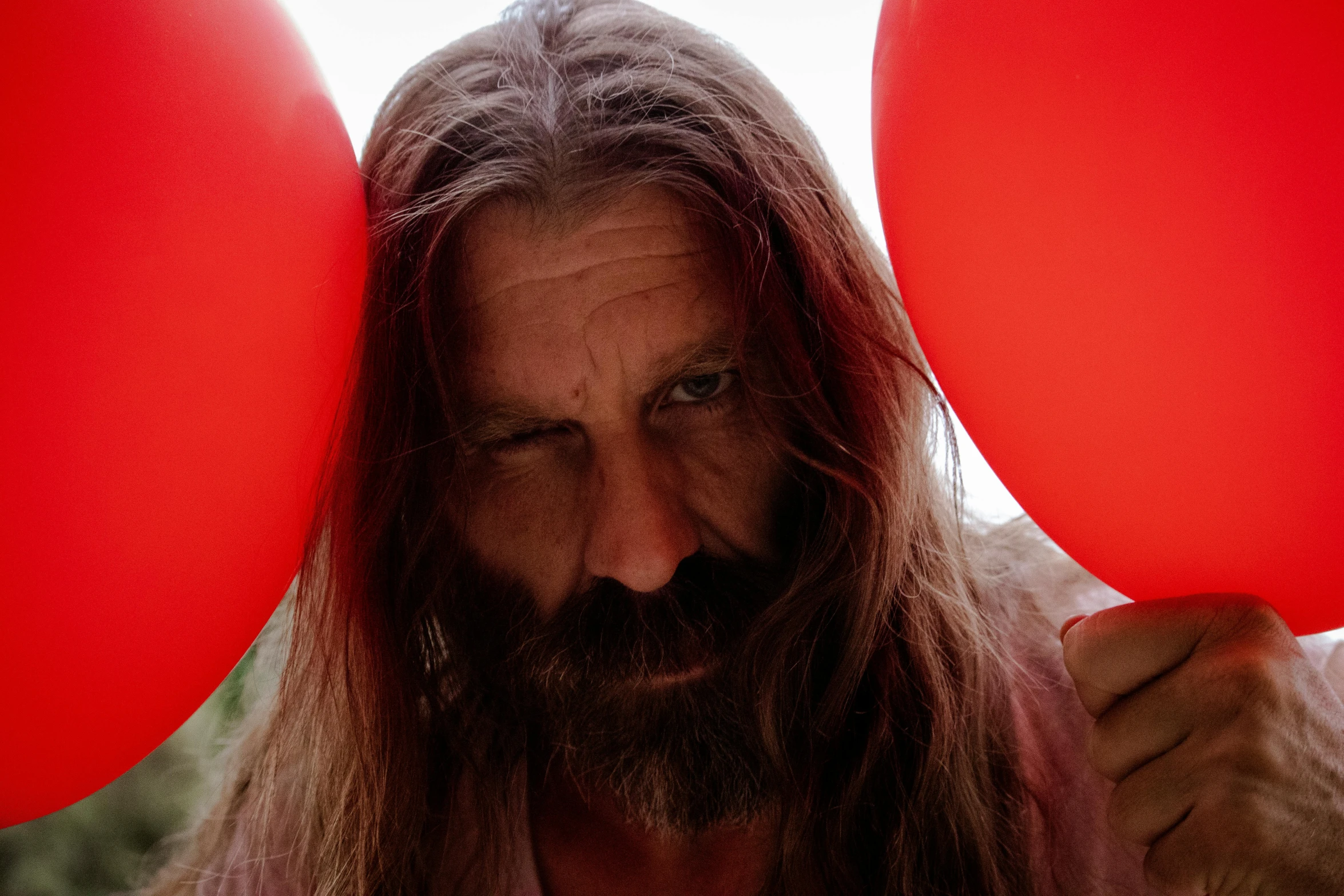 a man with long hair holding two large round red balloons