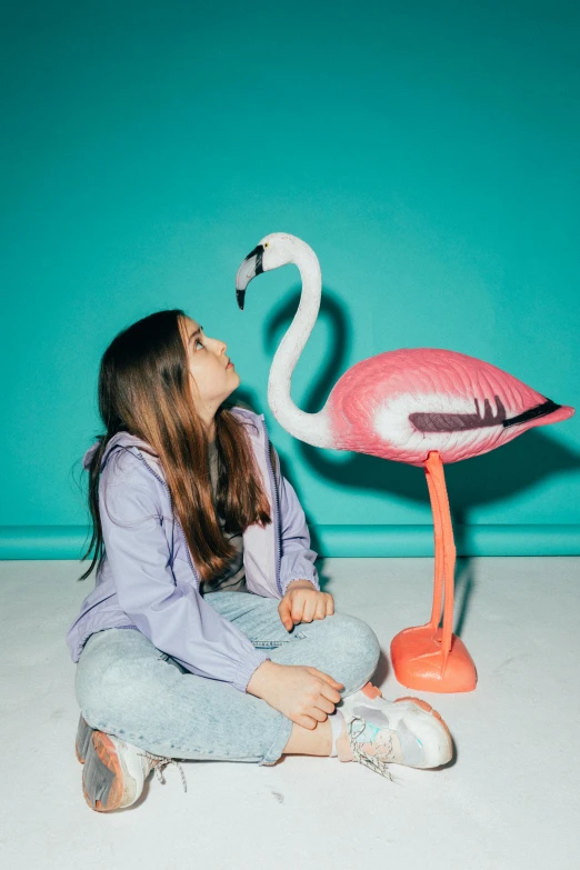 girl sitting next to fake pink flamingo on floor