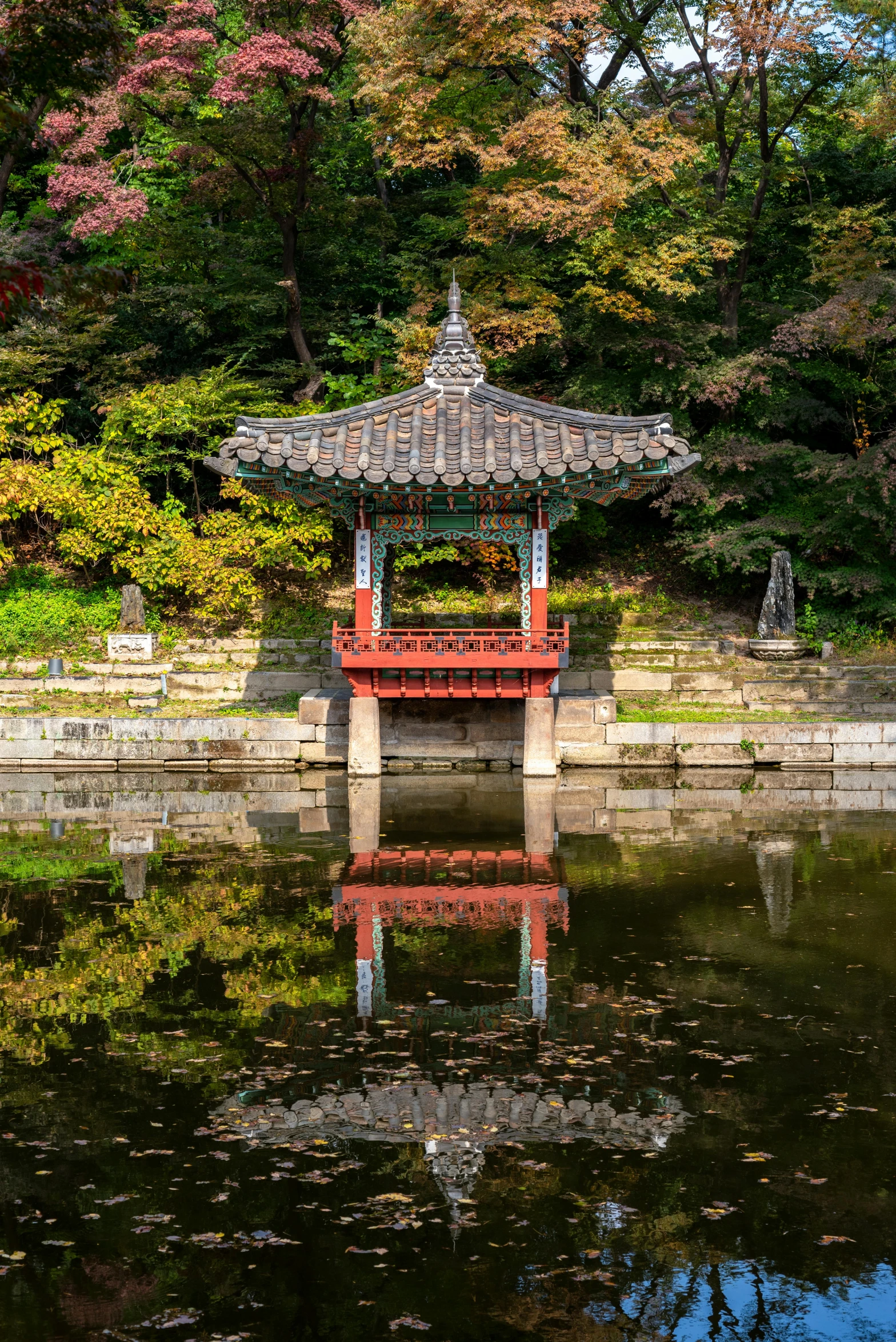 a red asian style gazebo in the water with fall colors