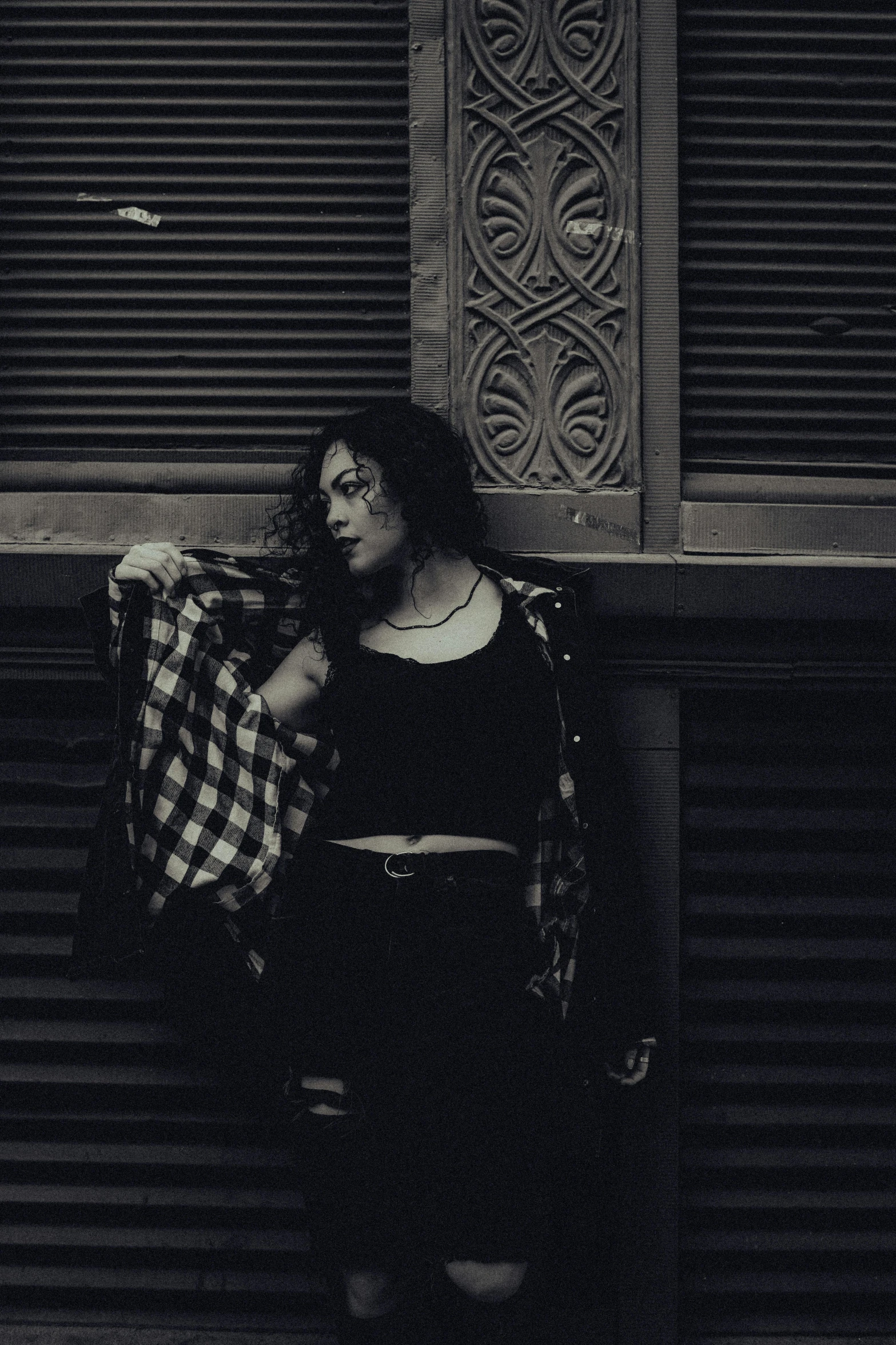 woman with plaid bags and black dress standing in front of a closed door