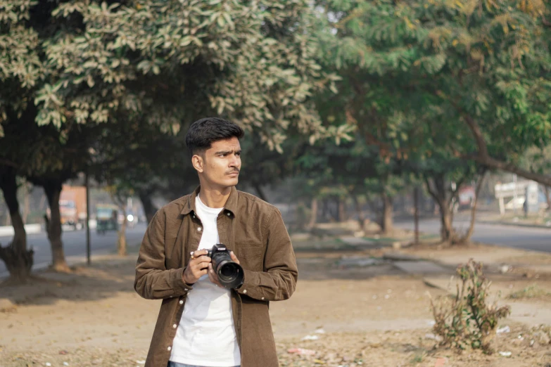 a young man holds up his camera near the trees