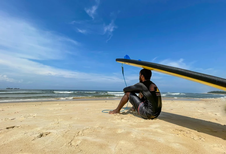 a man with a surfboard sits in the sand