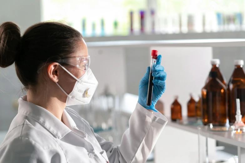 the woman in the lab wears a mask and glasses while holding a pipette