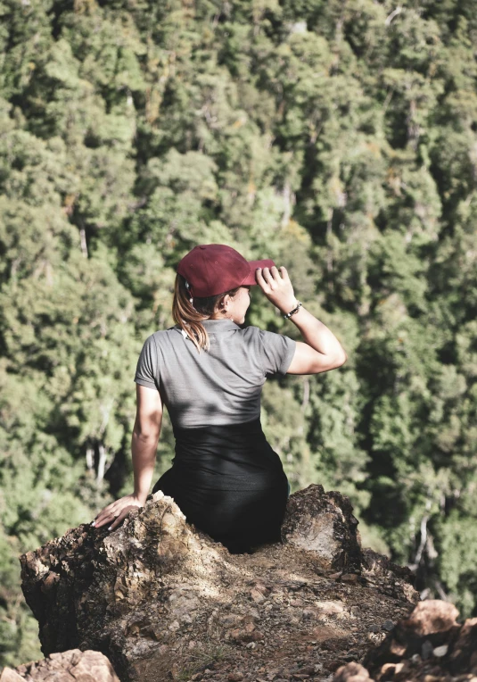 a woman is sitting on a rock looking out over the forest