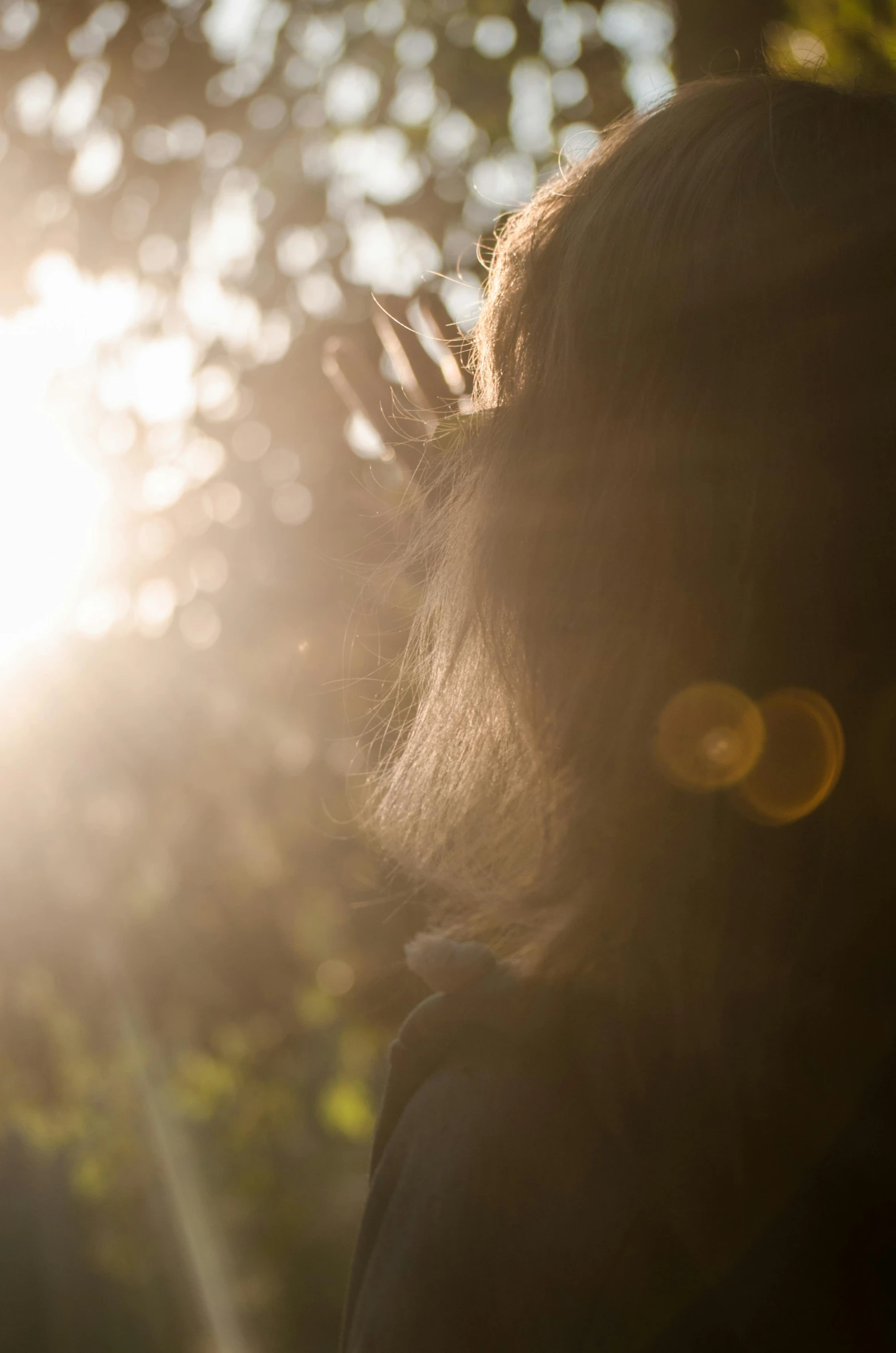 a woman standing in the sun light holding her hand up to her face